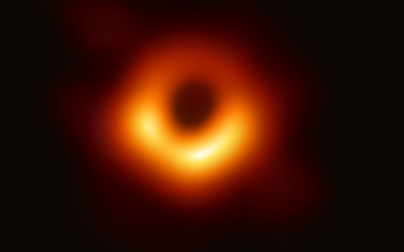 Primeira imagem de um buraco negro. É um círculo laranja em um fundo preto.
